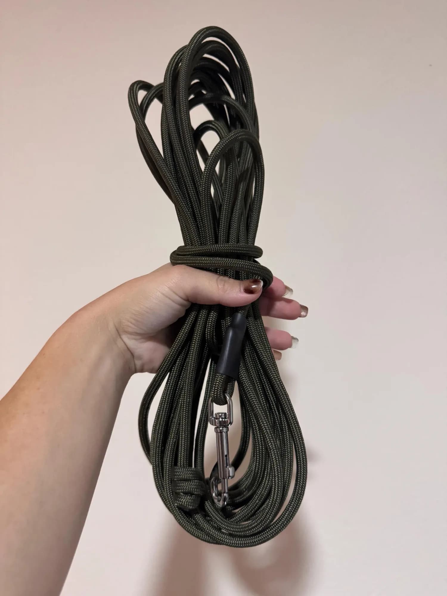 Hand holding a coiled dark green paracord long line with a snap clip, thumbnail